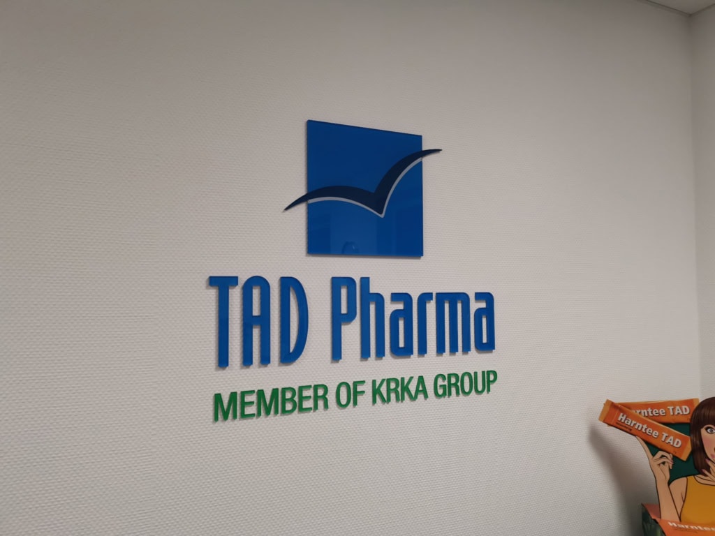 Moder in zelen 3D logotip TAD Pharma na steni.
