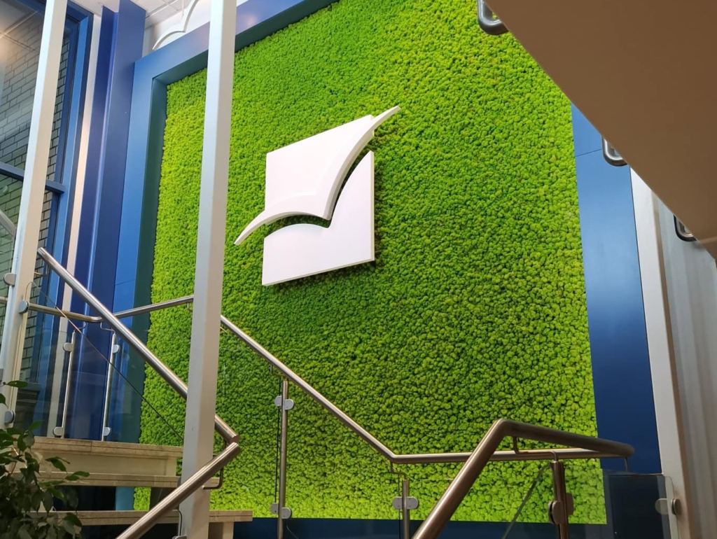 Velik bel 3D logotip TAD Pharma na zeleni steni ob stopnišču.